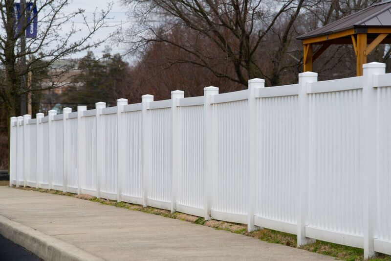 Tall white vinyl closed picket fence in six-foot panels along a sidewalk