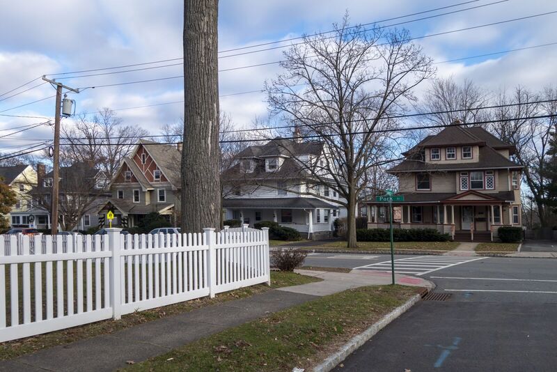 White vinyl straight picket fence wrapping a corner lot at a neighborhood crosswalk