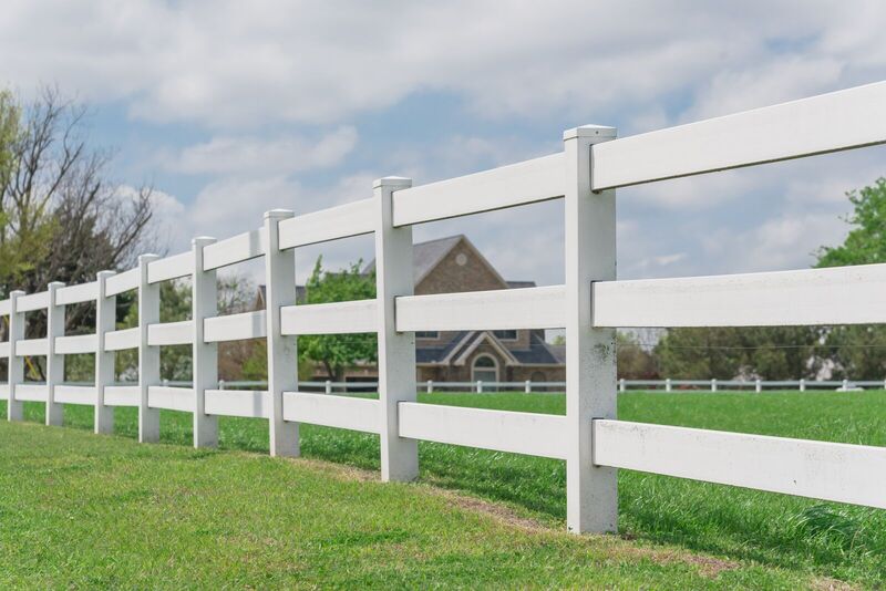 White vinyl three-rail ranch fence around a pasture with a home behind
