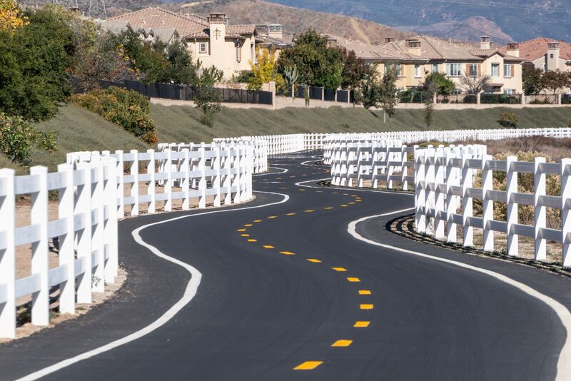 White vinyl three-rail ranch fence lining a curving roadway