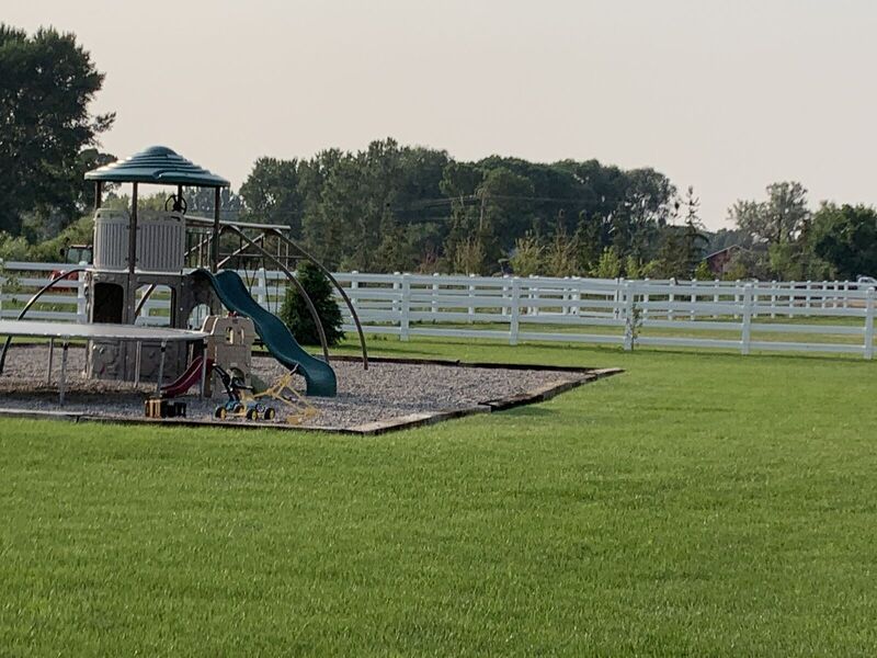 White vinyl four-rail ranch fence enclosing a lawn with a playset