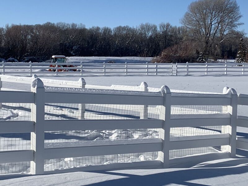 White vinyl four-rail ranch fence with wire mesh backing in snow